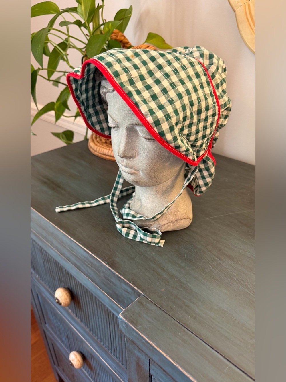 Green and White Gingham check bonnet with red trim along brim. Tie chin strap.